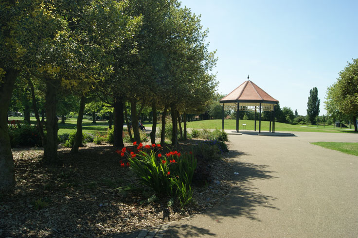 A wildflower bed with people on a bench behind it, and a bandstand on the right.
